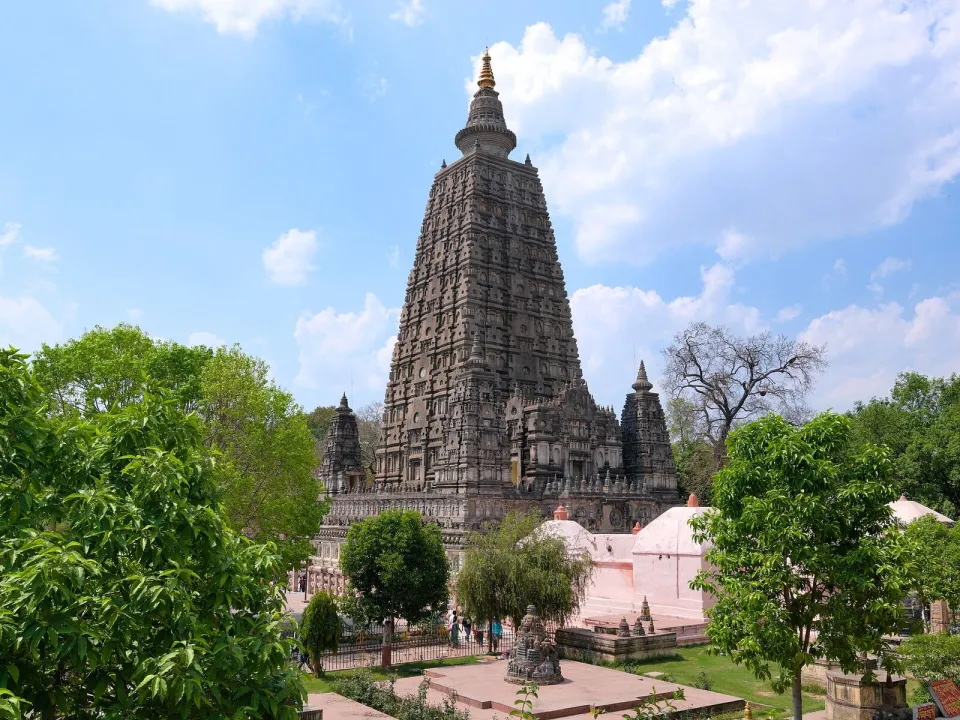 The tall stone tower of the Mahabodhi Temple at Bodh Gaya among green trees