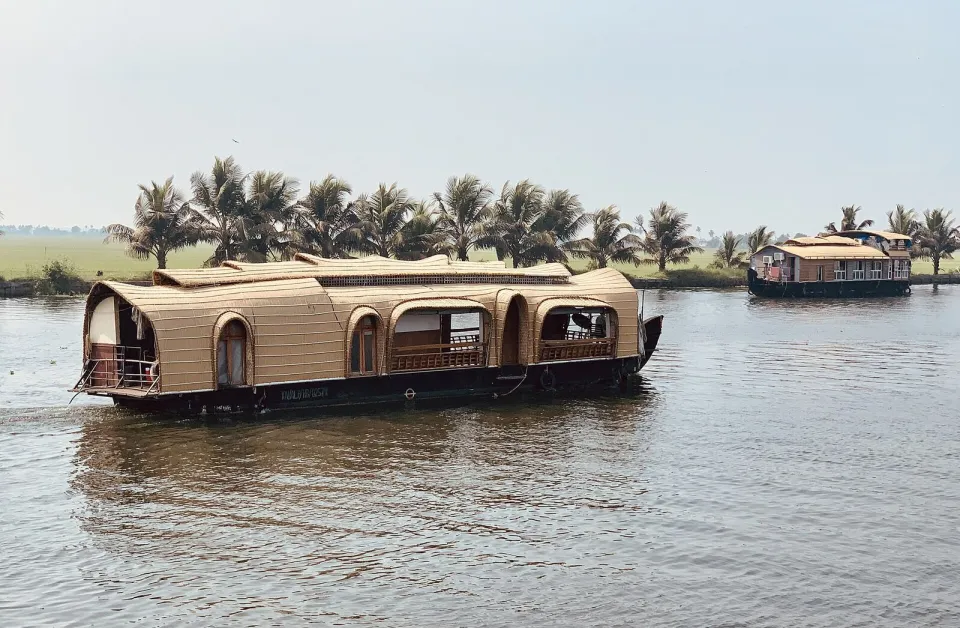 A thatched houseboat on the Kerala backwaters with coconut palms on the bank